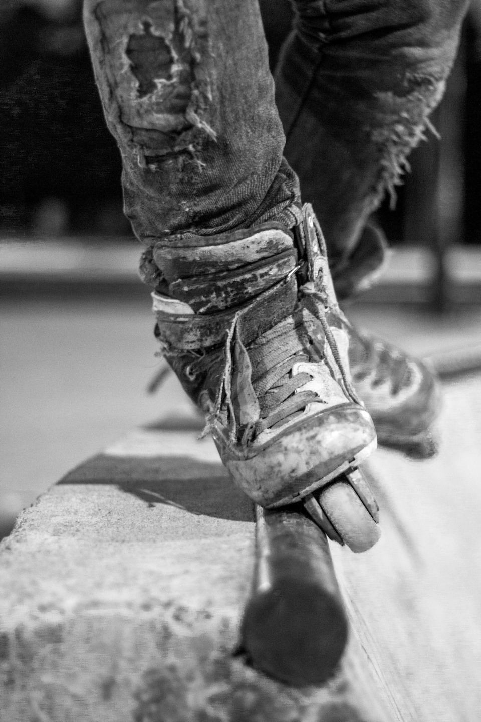 Black-and-white close-up of a heavily worn inline skate performing a rail grind, with distressed jeans and scuffed skate boots emphasizing street skating action and durability.
    